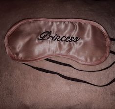 a sleeping mask with the word princess on it sitting on top of a brown blanket