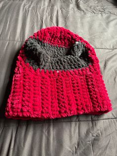 a crocheted hat laying on top of a bed next to a gray and red blanket