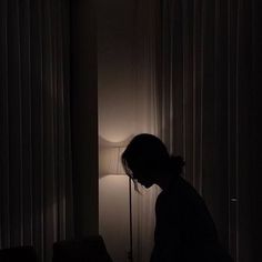 a person standing in front of a lamp next to a window with curtains on it