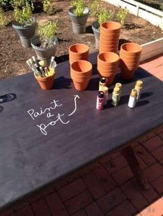 there are many pots on the table with paint bottles and markers written on them in white chalk