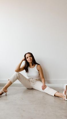 a woman is sitting on the floor with her legs crossed and wearing white shoes, smiling at the camera