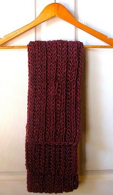 a red knitted scarf hanging on a wooden hanger next to a white wall