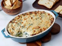 a blue casserole dish with cheese and spinach in it next to crackers