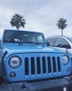 a blue jeep parked in a parking lot next to other cars and palm trees on a cloudy day