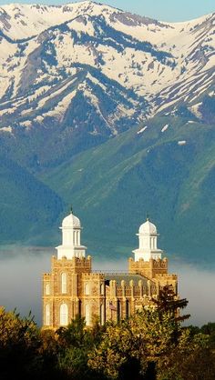 a large building with two towers in front of snow covered mountains and water below it