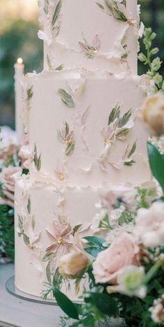 a white wedding cake with pink flowers and greenery on the side, surrounded by candles