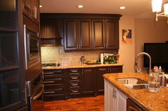 a kitchen with dark wood cabinets and marble counter tops, along with stainless steel appliances