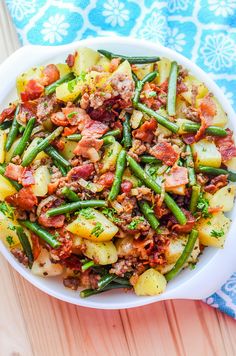 a white bowl filled with green beans, potatoes and other vegetables on top of a wooden table