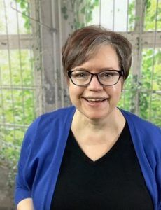 a woman wearing glasses standing in front of a caged area and smiling at the camera