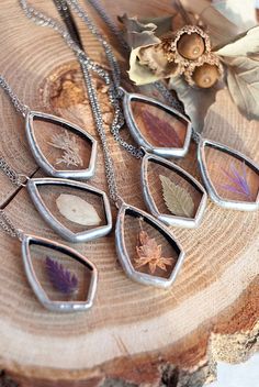 four necklaces with leaves on them sitting on top of a piece of tree bark