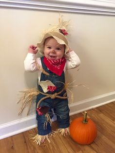 a small child in overalls and a cowboy hat standing next to a pumpkin on the floor