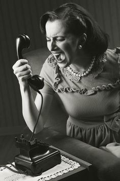 an old fashioned woman screaming while talking on the phone with her mouth open and holding a typewriter in front of her