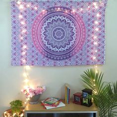 a purple and white tapestry hanging on the wall above a table with books, plants and lights