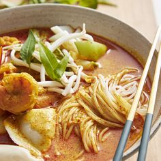 a bowl of soup with noodles, meat and vegetables in it next to chopsticks