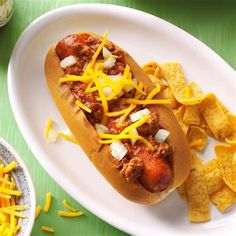 a chili dog with cheese and onions on a plate next to some potato wedges