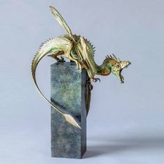 a bronze sculpture of a dragon on top of a green marble block with its tail curled up