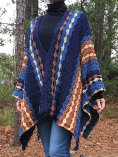 a woman is walking in the woods wearing a blue and brown ponchy shawl