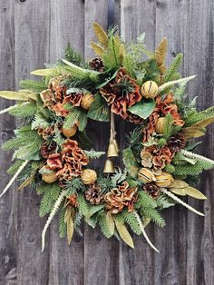 a wreath with pine cones and evergreen leaves on a wooden fence post, decorated with gold bells