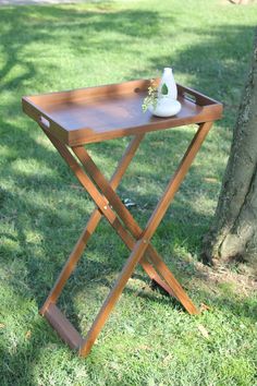 a wooden table with a vase on it sitting in the grass next to a tree