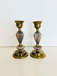 two gold colored candlesticks sitting next to each other on a white counter top