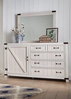 a white dresser with a mirror on top of it next to a rug and flowers