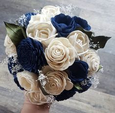 a bridal bouquet with blue and white flowers on a wooden table in front of a person's hand