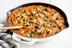 a pan filled with red sauce and spinach on top of a white tablecloth