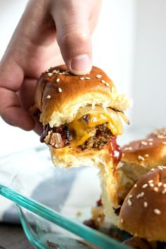 a hand holding a cheeseburger over a glass dish