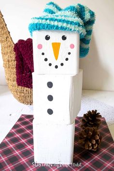 a wooden block with a snowman on it and a pine cone in the background