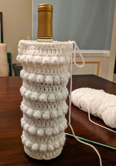 a crocheted wine bottle holder sitting on top of a wooden table