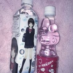 two water bottles sitting next to each other on a pink blanket, one with an anime character