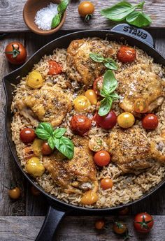 a skillet filled with chicken, tomatoes and rice on top of a wooden table