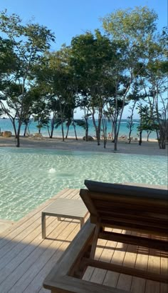 a wooden deck next to a swimming pool with trees in the background and blue water