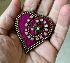 a heart shaped brooch in the palm of someone's hand