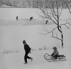 black and white photograph of two people pulling a sleigh in the snow with one person on it