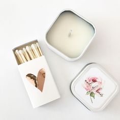 an open tin with matches and a candle in it on a white surface next to a box of matches