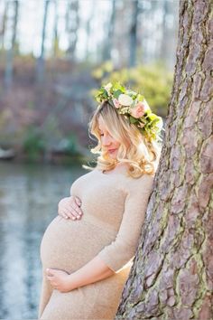 a pregnant woman leaning against a tree wearing a flower crown