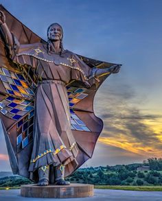 a statue of a woman with her arms outstretched in front of the sun set sky