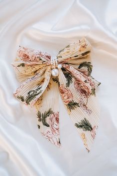 A bow for those who like to stand out! Our Find Me Bow features a unique floral print in pleated fabric with pearl center details, all on a classic french barrette. Add some pizzazz to any outfit--you won't be able to stay hidden with this head-turner! Approx. 6.5" x 9.5" Fabric bow French barrett clip Pale White Skin, Bow Designs, Classic Academia, French Barrette, Fabric Bows, Pleated Fabric, Contemporary Outfits, Bow Design, Makeup Bags