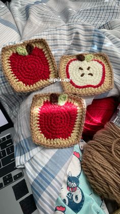 three crocheted apple coasters sitting on top of a bed next to a laptop