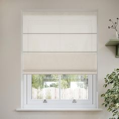 a window with white roman shades in a room next to a potted green plant