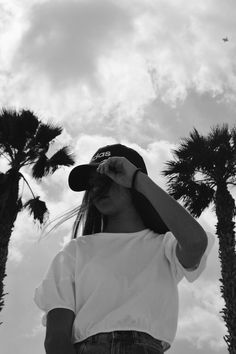 a woman standing in front of palm trees wearing a hat and looking at the sky