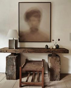 a wooden table sitting next to a lamp on top of a hard wood floor under a painting