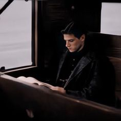 a man sitting on a train reading a book and looking at the paper in his hand