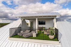 a small white house with a metal roof and black iron railings on the balcony