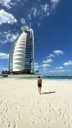 a man walking on top of a sandy beach next to the ocean with a tall building in the background