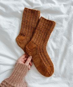 someone is holding up two brown knitted socks on top of a white bed sheet