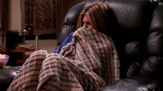 a woman wrapped up in a blanket sitting on a recliner with her eyes closed