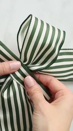 a person is tying a green and white striped bow on a piece of cloth with one hand