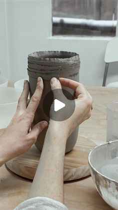 someone is making a vase out of clay on a table with bowls and plates around it